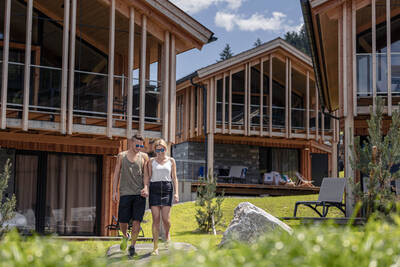 Man en vrouw wandelen tussen vakantiehuizen op Alps Resorts Bergresort Hauser Kaibling