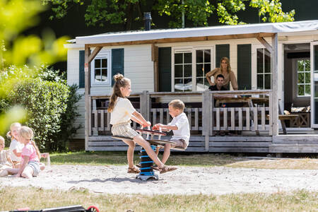 Kinderen spelen voor een chalet met overdekte veranda op vakantiepark Kampeerdorp de Zandstuve