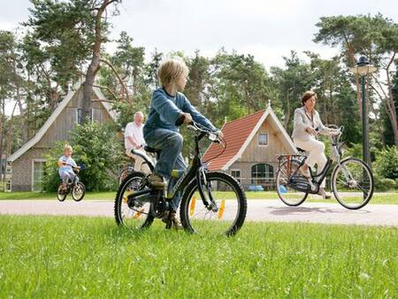 Gezin fiets langs vakantiehuizen op vakantiepark Landal De Hellendoornse Berg