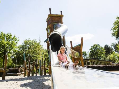 Kind glijdt van de glijbaan in een speeltuin op vakantiepark Landal Twenhaarsveld