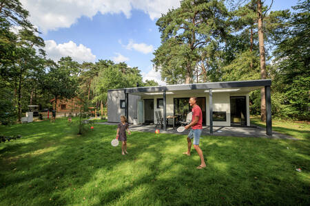 Vader en dochter tennissen in de tuin van en vakantiehuis op vakantiepark RCN het Grote Bos