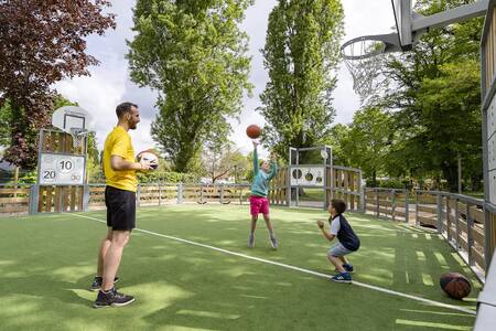 Vader met 2 kinderen spelen op het multifunctionele sportveld van Roompot Château des Marais